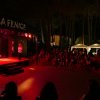 Spettacolo serale con pubblico seduto e palco illuminato, tenda con scritto 