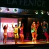 Gruppo di persone che ballano su un palco illuminato con scritta 