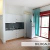 Bilocale con cucina, frigorifero, tende azzurre e balcone luminoso.