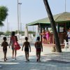 Persone camminano verso un chiosco all'aperto, accanto a tavoli e alberi.
