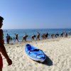 Spiaggia con bagnino, kayak blu e persone che fanno esercizi in fila vicino al mare.