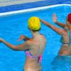 Due donne in piscina fanno esercizi con cuffie colorate, una gialla e l'altra rossa.