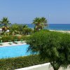 Una piscina con sdraio e ombrelloni, vista mare. Palme e vegetazione attorno.