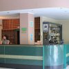Una reception d'hotel con due persone al bancone, scaffale per chiavi e piccolo bar sulla destra.
