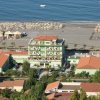 Hotel verde fronte spiaggia con lettini e ombrelloni sulla sabbia.