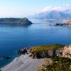 Vista panoramica su un promontorio e una lunga spiaggia con montagne in lontananza.