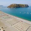 Spiaggia affollata di ombrelloni e lettini, isola verde sul mare.