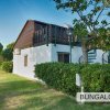 Bungalow bianco con tetto marrone, giardino e scale esterne in ferro.