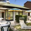 Giardino con tavolo, sedie, ombrelloni e lettino esterno accanto a un bungalow.