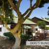 Un bungalow bianco con tetto verde, circondato da alberi e recinzioni in legno.