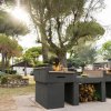 Un barbecue in pietra con legna sotto, situato in un'area verdeggiata.