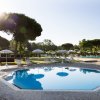 Piscina ottagonale all'aperto con sdraio e ombrelloni, circondata da alberi.