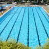 Piscina lunga con corsie e persone che nuotano, ombrelloni e lettini ai lati.