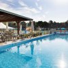 Piscina con area coperta per sedersi, ombrelloni e vegetazione attorno.