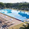 Ampia piscina olimpionica con corsie, circondata da ombrelloni e lettini, immersa nel verde.
