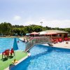 Piscina con ponte pedonale, circondata da sedie e tavoli sotto ombrelloni colorati.