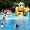 Persone giocano in piscina con scivoli colorati sullo sfondo.