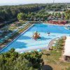 Vista dall'alto di piscina con ombrelloni blu, scivoli e tende bianche.