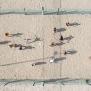Persone che giocano a pallavolo su un campo di sabbia, viste dall'alto.