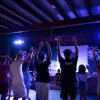 Persone ballano su un palco illuminato, con le mani alzate.