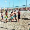 Bambini in pantaloncini da bagno sulla sabbia vicino a una rete.