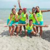 Sei persone sorridenti in uniforme gialla su una spiaggia.