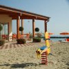 Giocattolo a molla su spiaggia, con terrazza all'aperto e ombrelloni arancioni sullo sfondo.