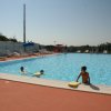 Piscina con bambini che nuotano e sdraio vuote intorno.
