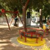 Un parco giochi con altalene, giostra girevole, e un bambino su un gioco a molla.