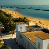 Vista panoramica di una spiaggia sabbiosa con ombrelloni, palme e edifici bianchi lungo il viale.