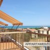 Vista dalla terrazza con tende da sole a strisce e tavoli bianchi, affacciata su tetti e mare.