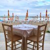 Tavolo apparecchiato su una terrazza vista mare, ombrelloni chiusi in lontananza.