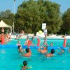 Persone giocano a pallavolo in piscina, con una rete gonfiabile e pubblico a bordo vasca.