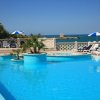 Piscina a bordo mare con lettini e ombrelloni blu e bianchi.