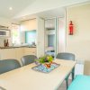 Sala da pranzo con tavolo, sedie, cucina, frigo e fiori al centro.