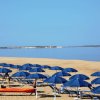 Spiaggia con ombrelloni blu e lettini, mare calmo sullo sfondo.