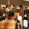 Prodotti alimentari e vino su un tavolo in un negozio. Due persone parlano sullo sfondo.
