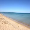 Una spiaggia deserta con sabbia chiara e acqua trasparente, cielo blu sopra.