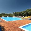 Piscina con scivolo giallo, lettini bianchi attorno e vegetazione sullo sfondo.