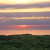 Sole al tramonto sopra un paesaggio di colline verdi e mare.